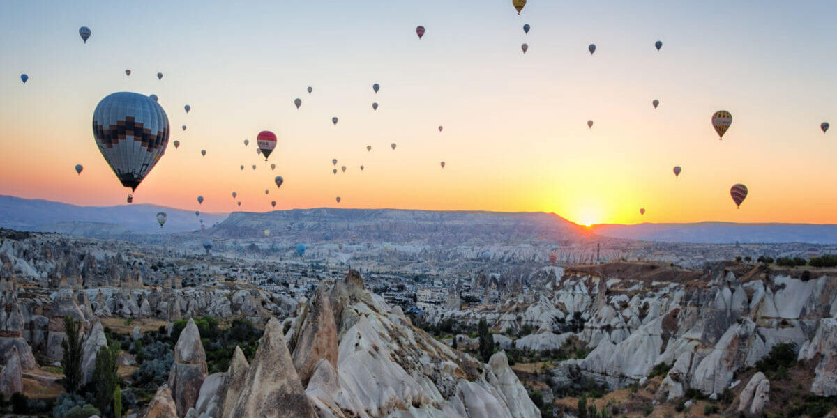 Hot air balloons floating at sunrise over the rocky valleys and fairy chimneys of Cappadocia, Nevşehir, Turkey.