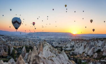 Hot air balloons floating at sunrise over the rocky valleys and fairy chimneys of Cappadocia, Nevşehir, Turkey.