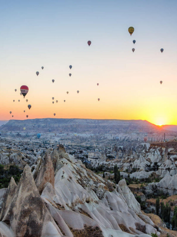 Hot air balloons floating at sunrise over the rocky valleys and fairy chimneys of Cappadocia, Nevşehir, Turkey.
