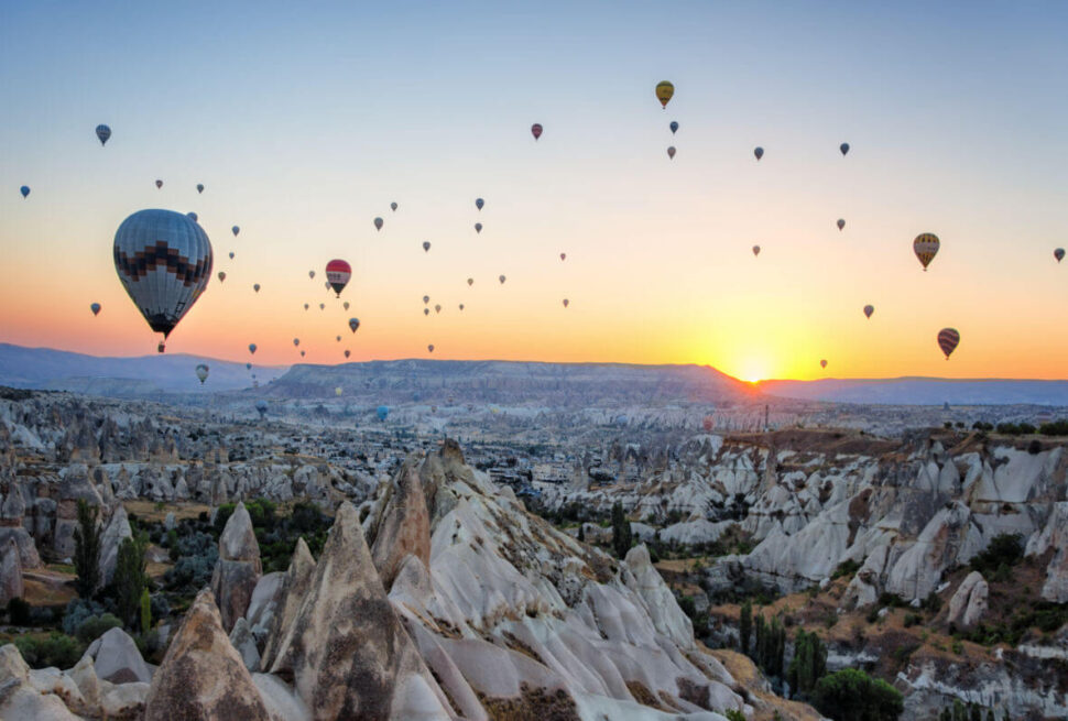 Hot air balloons floating at sunrise over the rocky valleys and fairy chimneys of Cappadocia, Nevşehir, Turkey.