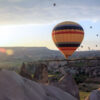 Vibrant hot air balloon floating at sunrise over Cappadocia’s rocky landscape and fairy chimneys in Turkey.