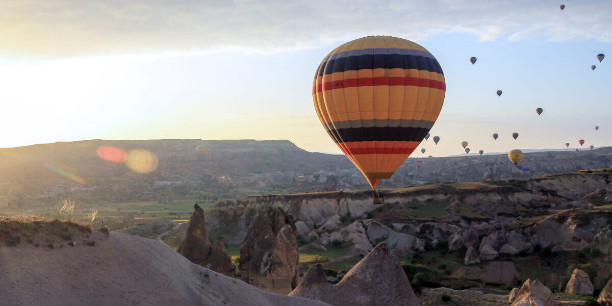 Vibrant hot air balloon floating at sunrise over Cappadocia’s rocky landscape and fairy chimneys in Turkey.