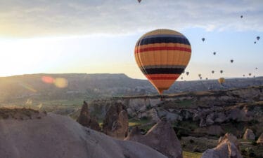 Vibrant hot air balloon floating at sunrise over Cappadocia’s rocky landscape and fairy chimneys in Turkey.