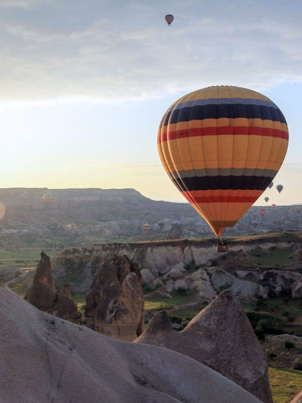 Vibrant hot air balloon floating at sunrise over Cappadocia’s rocky landscape and fairy chimneys in Turkey.