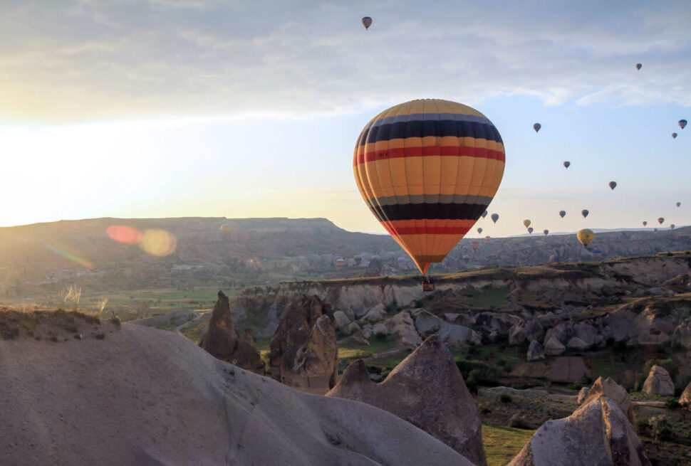 Vibrant hot air balloon floating at sunrise over Cappadocia’s rocky landscape and fairy chimneys in Turkey.