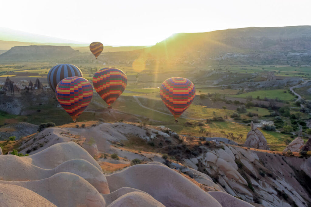 Colorful hot air balloons soaring above Cappadocia’s green valleys and fairy chimneys at sunrise in Turkey.
