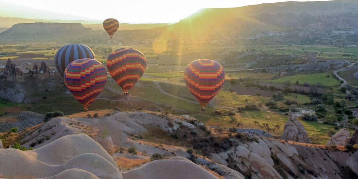 Colorful hot air balloons soaring above Cappadocia’s green valleys and fairy chimneys at sunrise in Turkey.