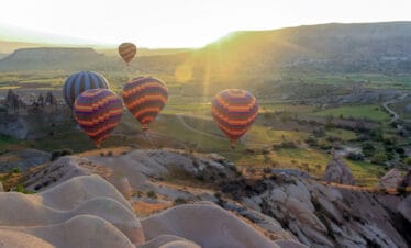 Colorful hot air balloons soaring above Cappadocia’s green valleys and fairy chimneys at sunrise in Turkey.