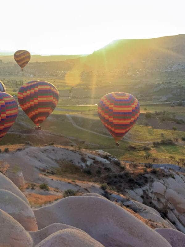 Colorful hot air balloons soaring above Cappadocia’s green valleys and fairy chimneys at sunrise in Turkey.
