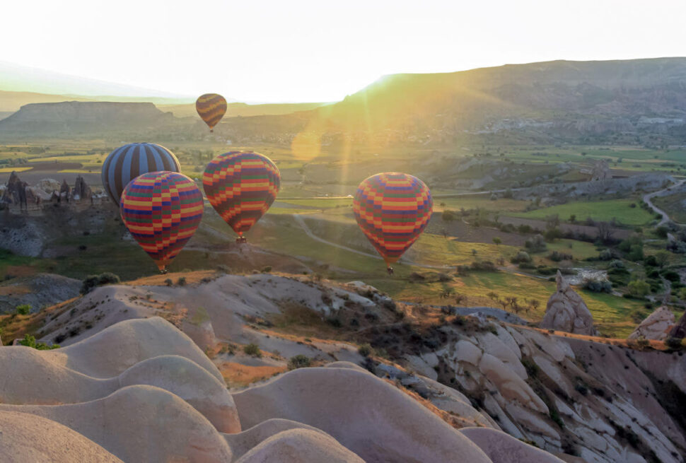 Colorful hot air balloons soaring above Cappadocia’s green valleys and fairy chimneys at sunrise in Turkey.