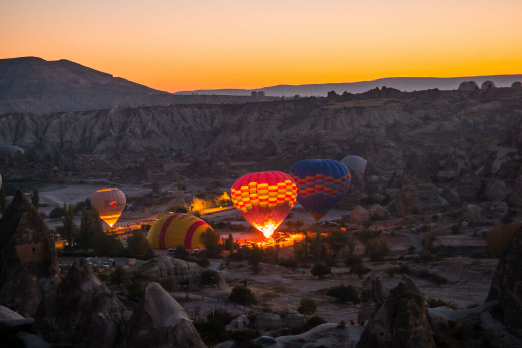 Hot air balloons inflating at dawn in Cappadocia, silhouetted against a soft pink and orange sunrise sky.