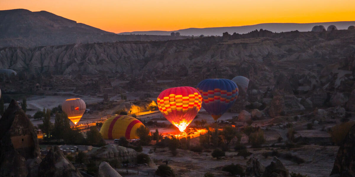 Hot air balloons inflating at dawn in Cappadocia, silhouetted against a soft pink and orange sunrise sky.