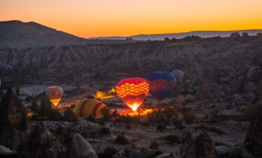 Hot air balloons inflating at dawn in Cappadocia, silhouetted against a soft pink and orange sunrise sky.