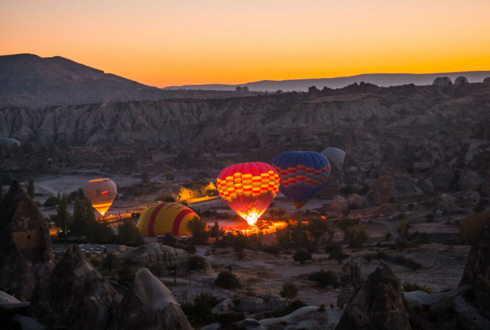 Hot air balloons inflating at dawn in Cappadocia, silhouetted against a soft pink and orange sunrise sky.