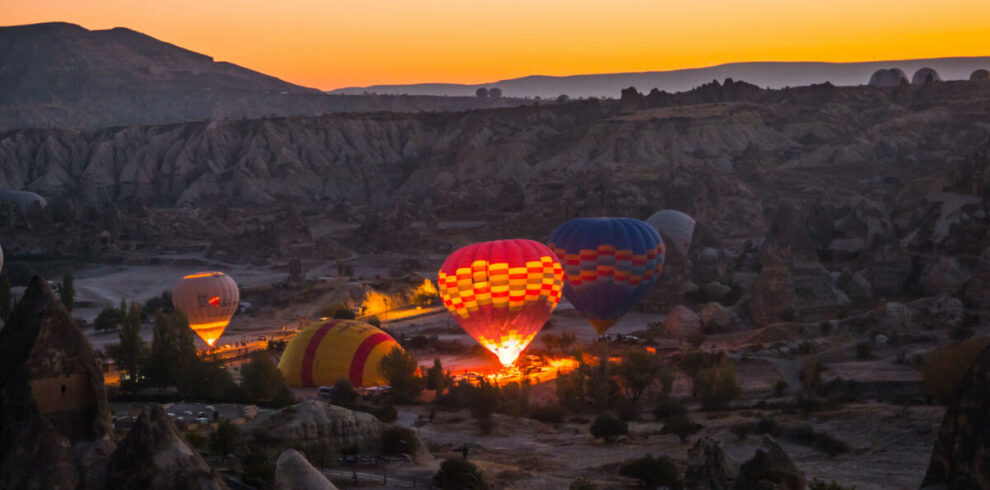 Hot air balloons inflating at dawn in Cappadocia, silhouetted against a soft pink and orange sunrise sky.