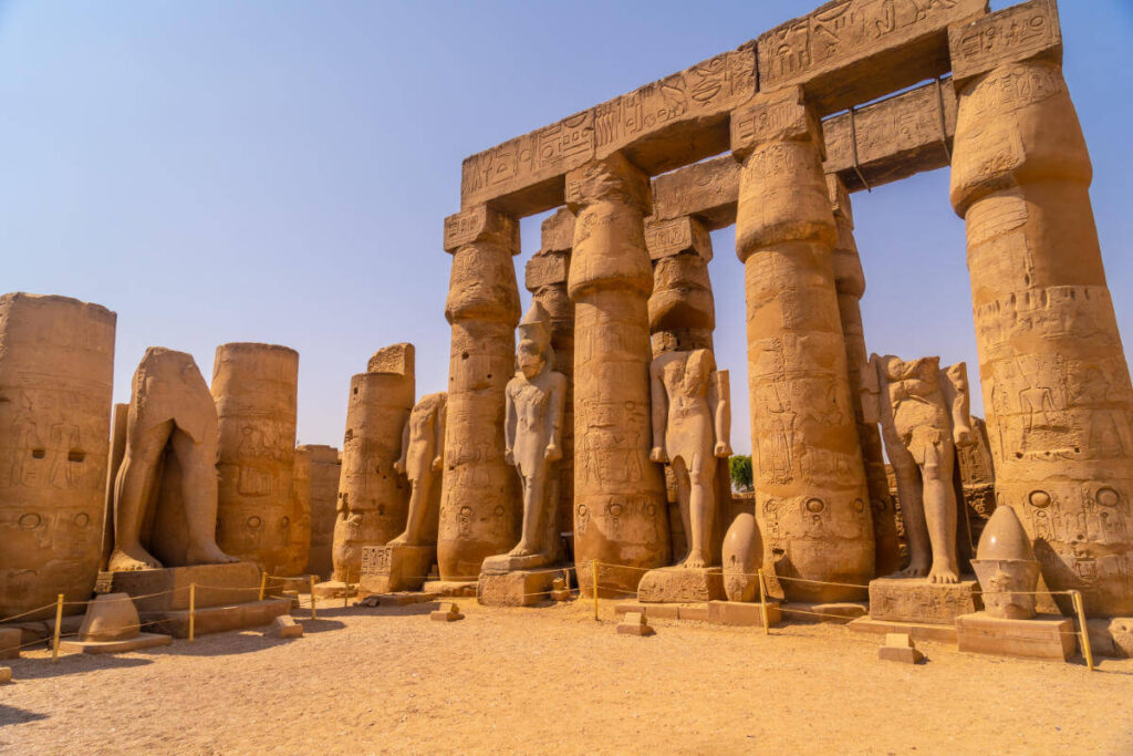 Ancient statues and massive carved columns in Luxor Temple, Egypt, showcasing hieroglyphics and pharaonic figures under a clear sky.