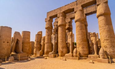 Ancient statues and massive carved columns in Luxor Temple, Egypt, showcasing hieroglyphics and pharaonic figures under a clear sky.