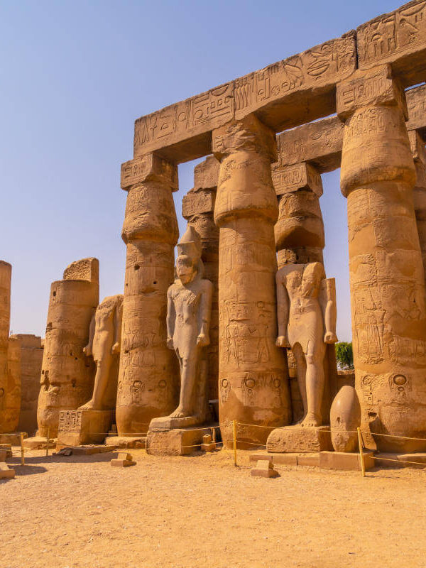 Ancient statues and massive carved columns in Luxor Temple, Egypt, showcasing hieroglyphics and pharaonic figures under a clear sky.