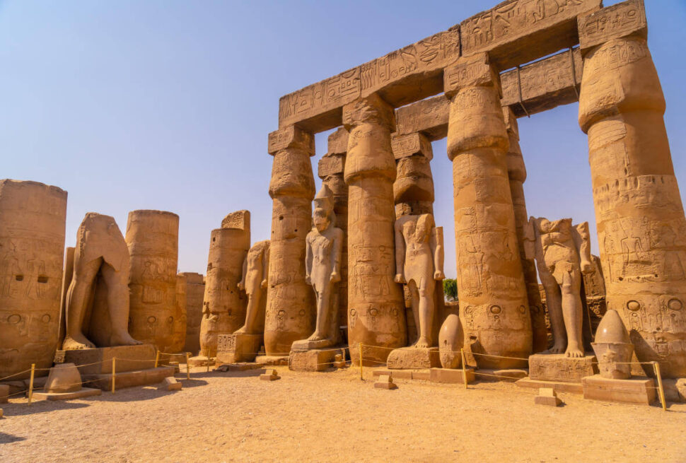 Ancient statues and massive carved columns in Luxor Temple, Egypt, showcasing hieroglyphics and pharaonic figures under a clear sky.