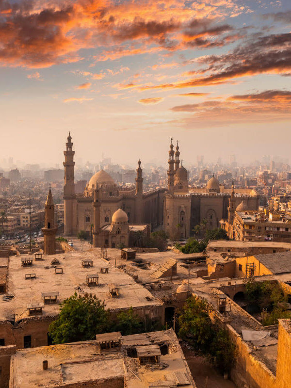 Skyline of Cairo, Egypt at sunrise with historic mosques and minarets surrounded by dense urban architecture and colorful clouds.