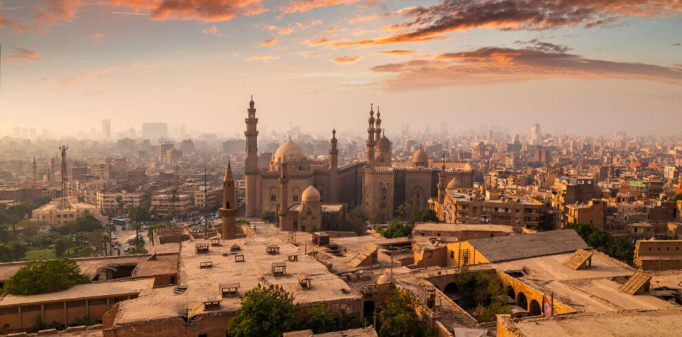 Skyline of Cairo, Egypt at sunrise with historic mosques and minarets surrounded by dense urban architecture and colorful clouds.