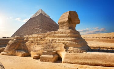 The Great Sphinx of Giza with the Pyramid of Khafre in the background, set against a clear blue sky in the Egyptian desert.