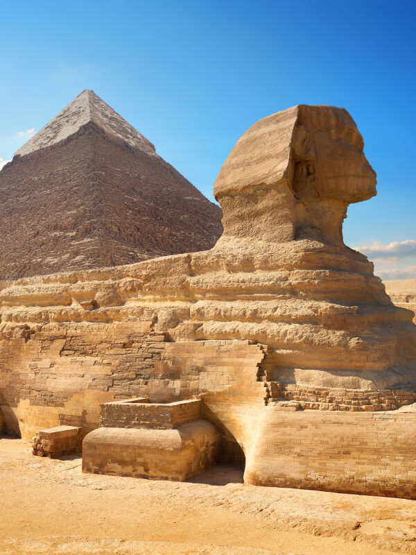 The Great Sphinx of Giza with the Pyramid of Khafre in the background, set against a clear blue sky in the Egyptian desert.