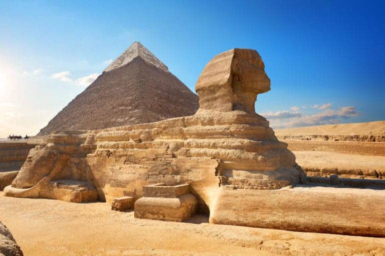 The Great Sphinx of Giza with the Pyramid of Khafre in the background, set against a clear blue sky in the Egyptian desert.