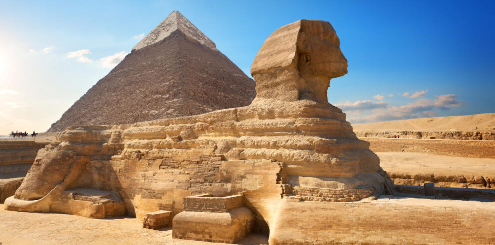 The Great Sphinx of Giza with the Pyramid of Khafre in the background, set against a clear blue sky in the Egyptian desert.