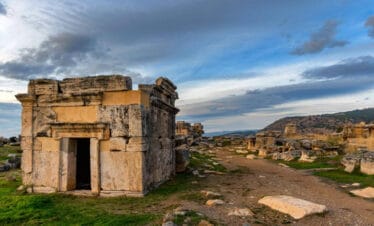 Ancient stone tomb structure in the necropolis of Hierapolis, Pamukkale, with dramatic skies and scattered ruins.