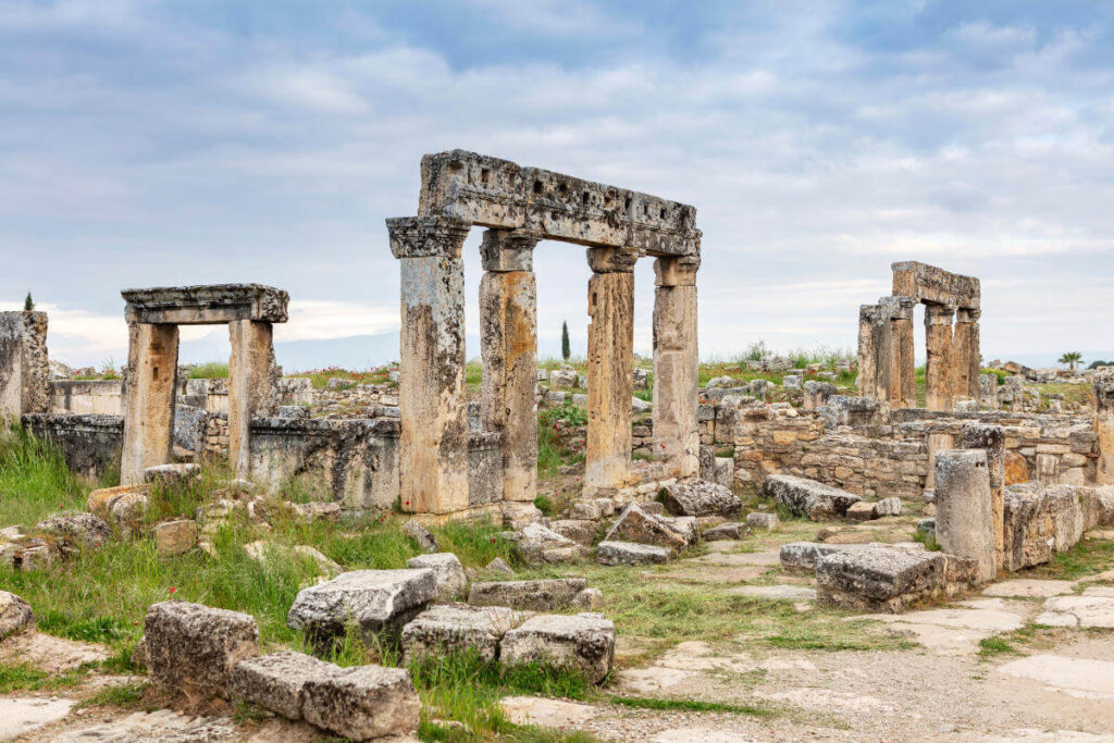 Ancient stone columns and scattered ruins in the necropolis of Hierapolis, Pamukkale, surrounded by wild greenery.