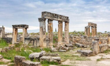 Ancient stone columns and scattered ruins in the necropolis of Hierapolis, Pamukkale, surrounded by wild greenery.