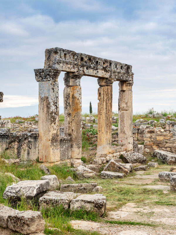 Ancient stone columns and scattered ruins in the necropolis of Hierapolis, Pamukkale, surrounded by wild greenery.