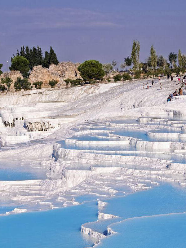 Blue thermal pools cascading down white travertine terraces in Pamukkale, Turkey, with tourists exploring the site.