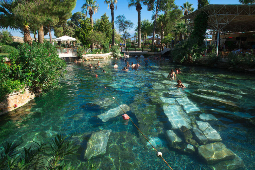 Tourists swimming in the ancient thermal waters of Cleopatra's Pool in Pamukkale, Turkey, surrounded by ruins.