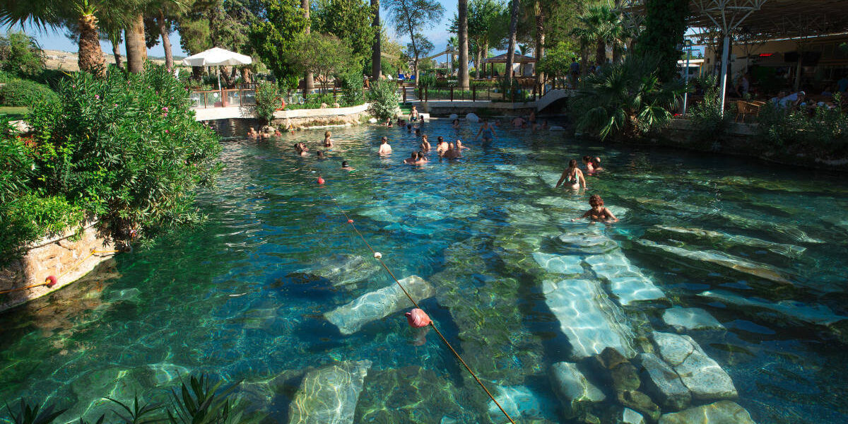 Tourists swimming in the ancient thermal waters of Cleopatra's Pool in Pamukkale, Turkey, surrounded by ruins.