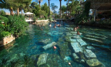 Tourists swimming in the ancient thermal waters of Cleopatra's Pool in Pamukkale, Turkey, surrounded by ruins.