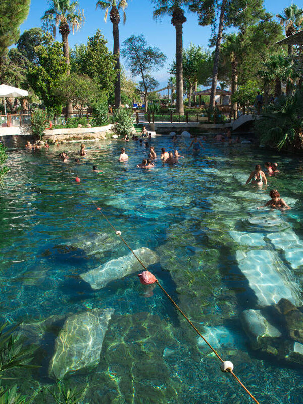 Tourists swimming in the ancient thermal waters of Cleopatra's Pool in Pamukkale, Turkey, surrounded by ruins.