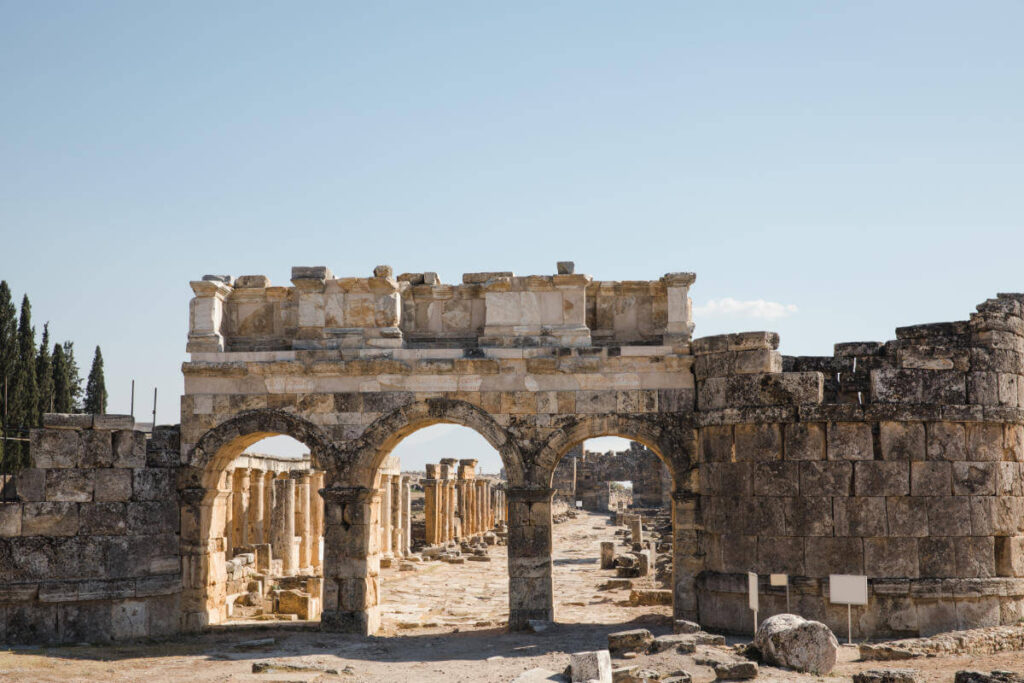 Ancient Roman gate with triple arch design in Hierapolis ruins, Pamukkale, Turkey under clear blue sky.