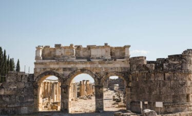 Ancient Roman gate with triple arch design in Hierapolis ruins, Pamukkale, Turkey under clear blue sky.