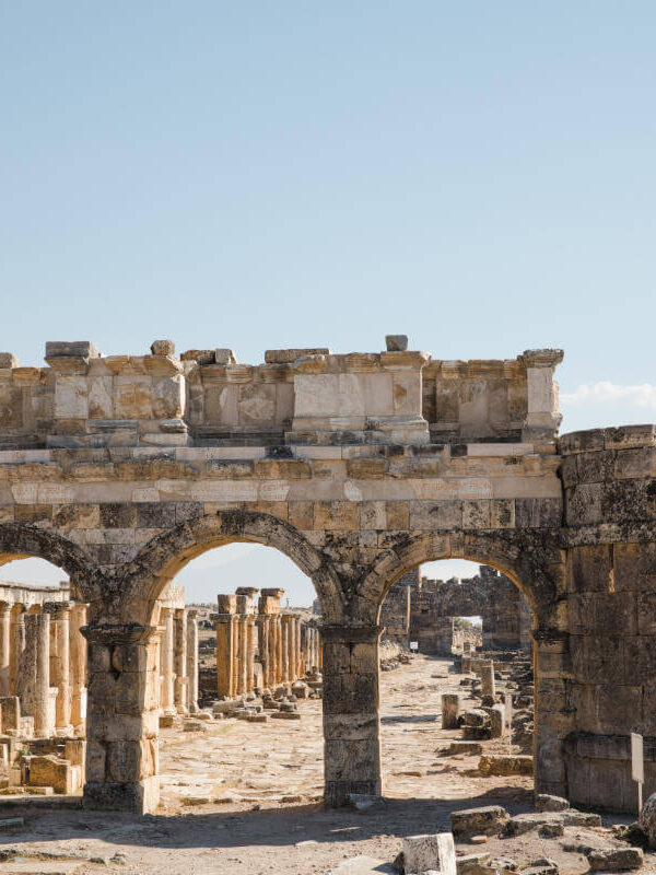 Ancient Roman gate with triple arch design in Hierapolis ruins, Pamukkale, Turkey under clear blue sky.