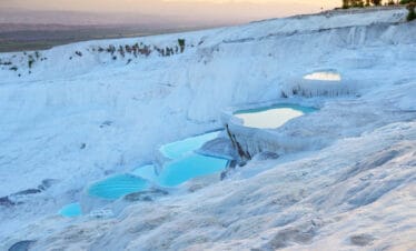 Golden sunset light reflects on Pamukkale's terraced thermal pools with white travertines and turquoise waters in Turkey.