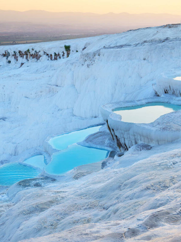 Golden sunset light reflects on Pamukkale's terraced thermal pools with white travertines and turquoise waters in Turkey.
