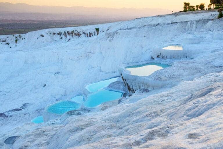 Golden sunset light reflects on Pamukkale's terraced thermal pools with white travertines and turquoise waters in Turkey.