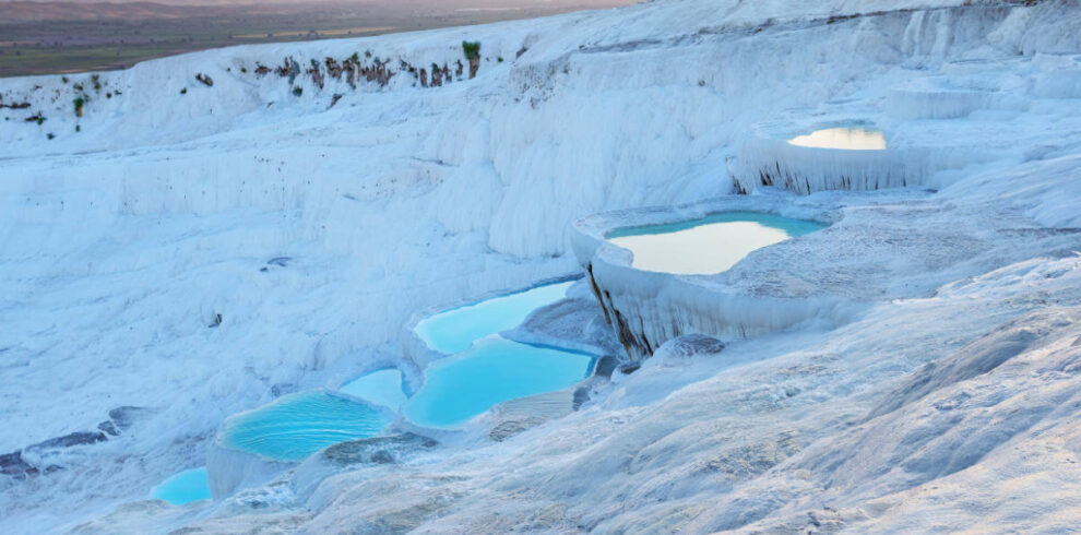 Golden sunset light reflects on Pamukkale's terraced thermal pools with white travertines and turquoise waters in Turkey.
