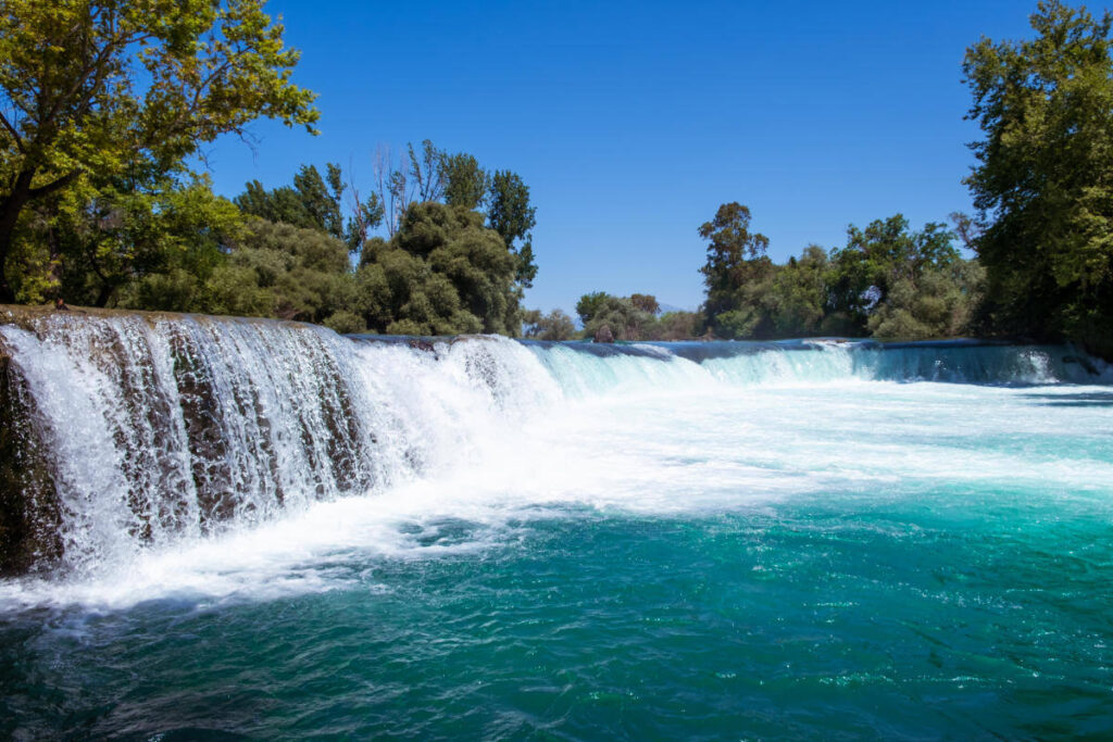 Scenic view of Manavgat Waterfall in Antalya, Turkey, with turquoise waters flowing over a wide rock ledge.