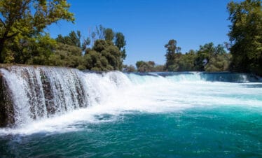 Scenic view of Manavgat Waterfall in Antalya, Turkey, with turquoise waters flowing over a wide rock ledge.