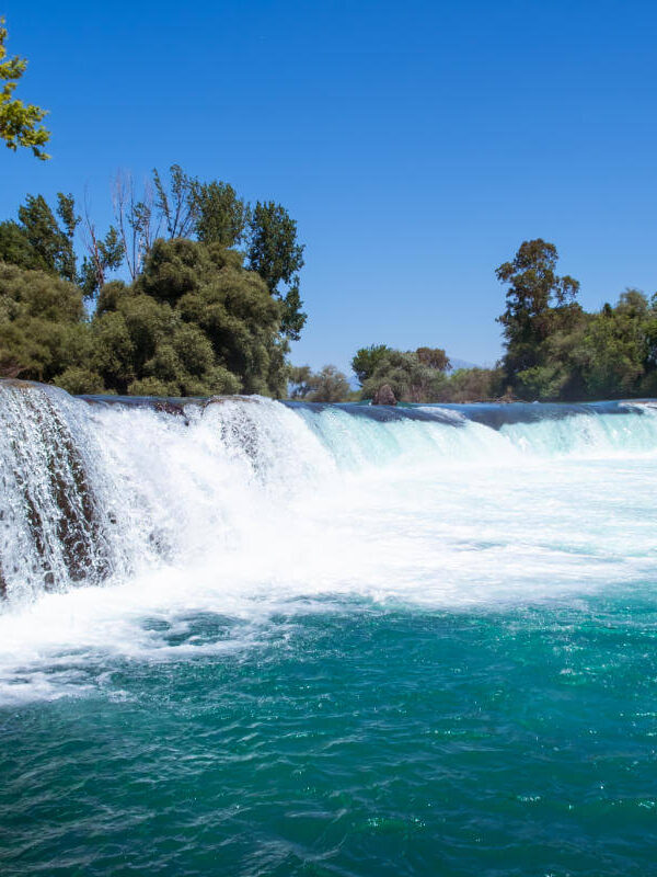 Scenic view of Manavgat Waterfall in Antalya, Turkey, with turquoise waters flowing over a wide rock ledge.