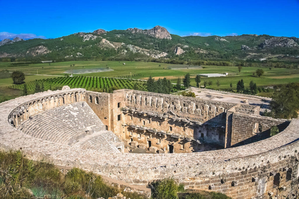 Well-preserved Roman Theatre of Aspendos in Antalya, Turkey, surrounded by green fields and distant mountains.