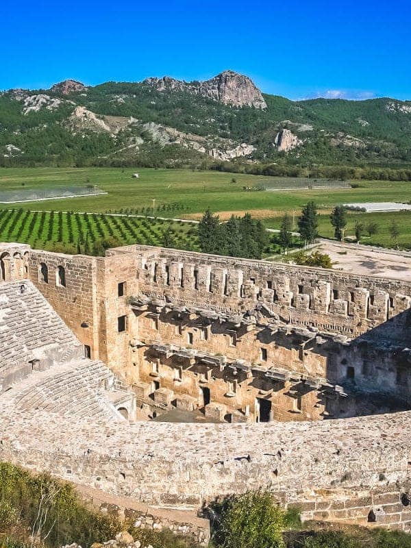 Well-preserved Roman Theatre of Aspendos in Antalya, Turkey, surrounded by green fields and distant mountains.